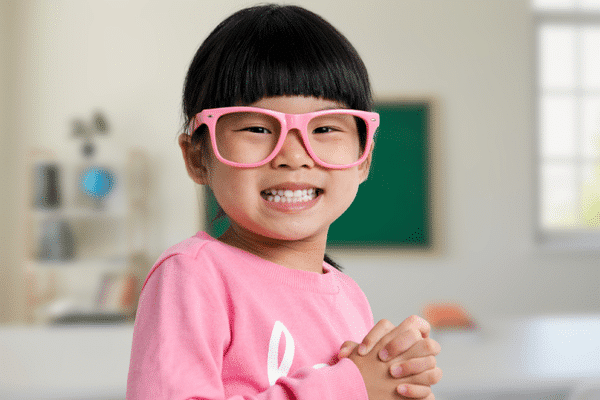 Young girl with pink glasses holding clear aligner | Troy City Orthodontics in Fall River, MA