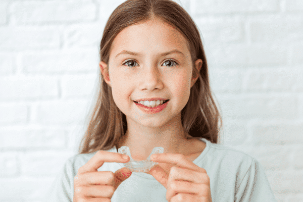 Preteen girl smiling holding clear aligner tray | Troy City Orthodontics in Fall River, MA