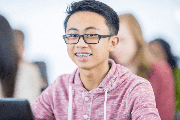 Teen boy with glasses smiling in pink hoodie | Troy City Orthodontics in Fall River, MA